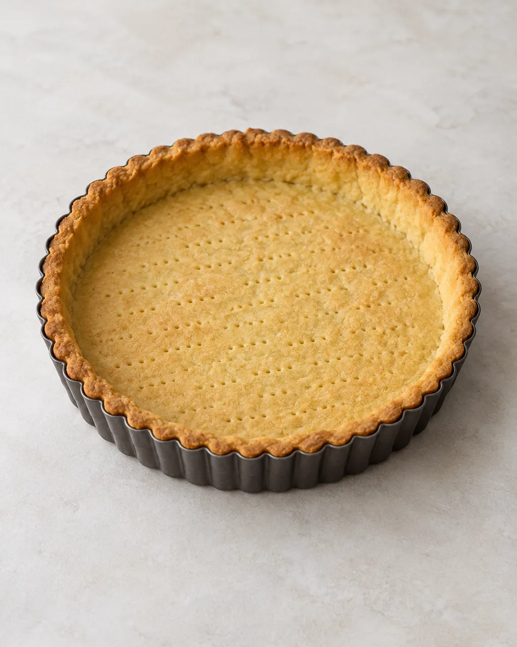 Base di pasta frolla dorata e friabile cotta in uno stampo da crostata.